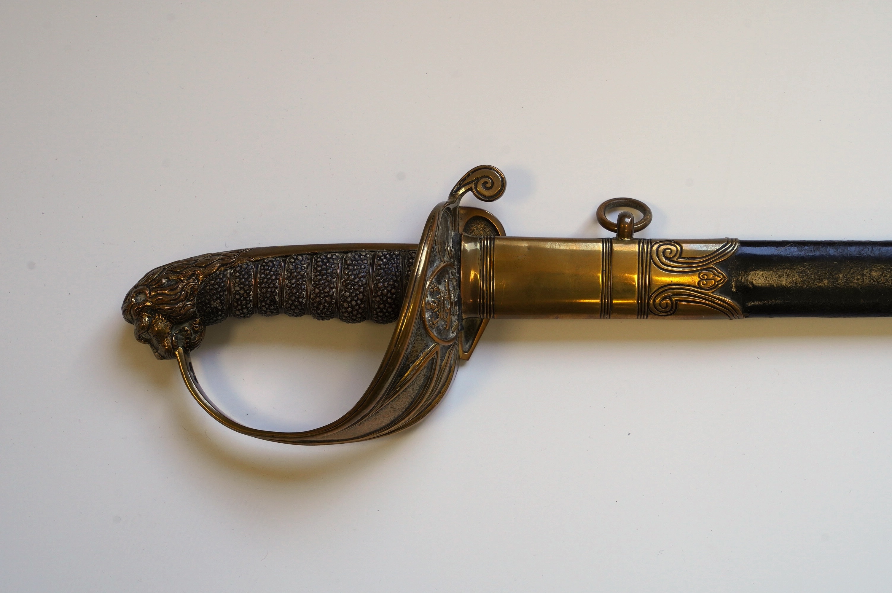 An early 19th century Royal Navy officer's sword with engraved blade, folding knuckle guard, lion’s head pommel and shagreen grip, leather scabbard with brass fittings, blade 73.5cm. Condition - fair, some wear overall.